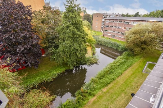 A tranquil urban scene showcasing a lush green park with a meandering waterway, surrounded by residential buildings and vibrant trees.