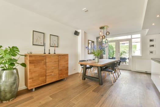 A stylish modern dining room featuring wooden furniture, decorative plants, and natural lighting, creating a warm and inviting atmosphere for gatherings.