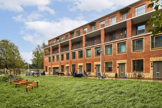 A contemporary red brick apartment building surrounded by lush green grass and trees, providing a peaceful outdoor space for residents.