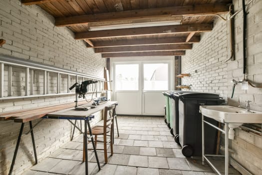 A spacious utility room featuring wooden beams, work tables, and modern waste bins, creating a functional and organized environment.