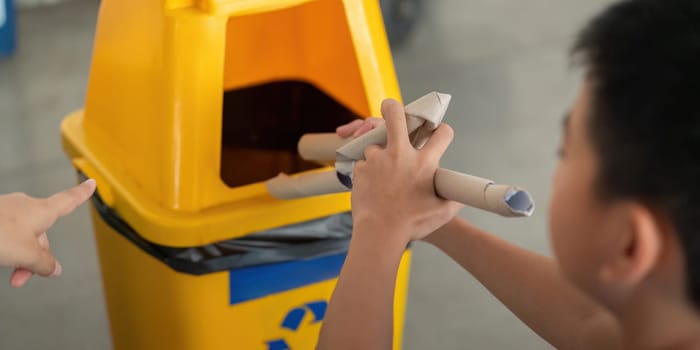 A young boy holds rolled-up cardboard, learning to recycle as he interacts with his mother, showcasing the importance of sustainable waste disposal practices.
