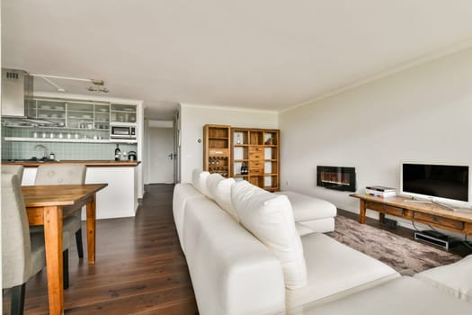 A stylish and modern living room featuring a wooden dining table, elegant furniture, and a sleek television setup in a bright minimalist space.