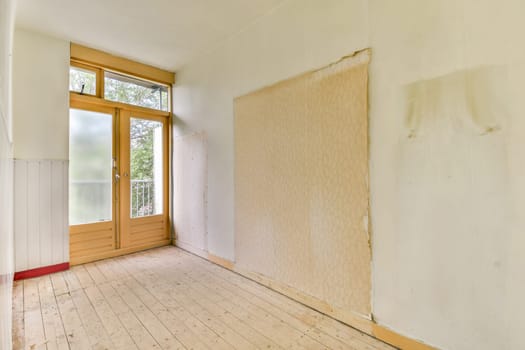 A vacant room featuring pale walls and a large window that allows natural light to fill the space. The floor is wooden, enhancing the minimalist aesthetic.