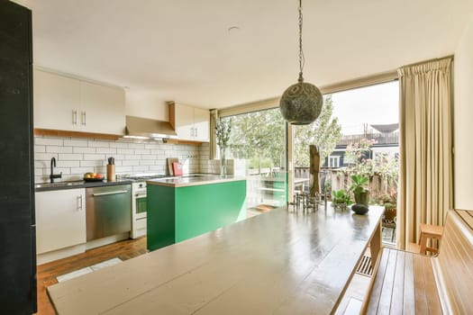 A stylish kitchen showcasing a blend of green cabinetry, sleek appliances, and abundant natural light through large windows, perfect for contemporary living.