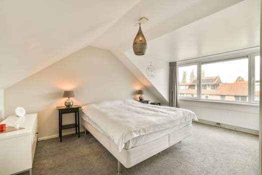 A stylish, well-lit bedroom featuring a comfortable bed, bedside table, and a large window with a scenic view, promoting a serene atmosphere.