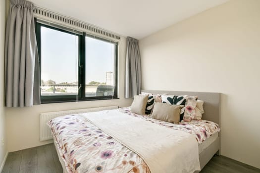A serene modern bedroom featuring a cozy bed adorned with floral bedding and decorative pillows, illuminated by ample natural light from a large window.