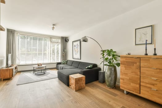 A stylish living room featuring a comfortable sofa, a wooden chest, large windows for natural light, and tasteful decor that creates a cozy atmosphere.