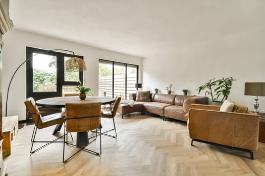 A stylish modern living room featuring a cozy leather sofa, a wooden dining table, and lush indoor plants, combining comfort with contemporary design aesthetics.