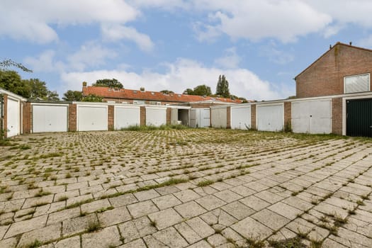 The image depicts a deserted garage area surrounded by overgrown vegetation and an uneven cobblestone surface, creating an eerie yet intriguing atmosphere.