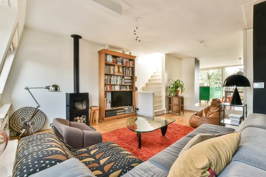 A stylish modern living room featuring a cozy seating area, bookshelves, and natural light flowing through large windows, creating an inviting atmosphere.
