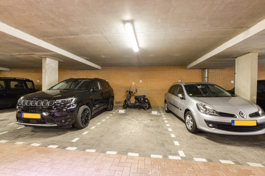 An indoor parking garage featuring a black SUV, a silver car, and a scooter. The environment highlights organized parking spaces with clear lines.