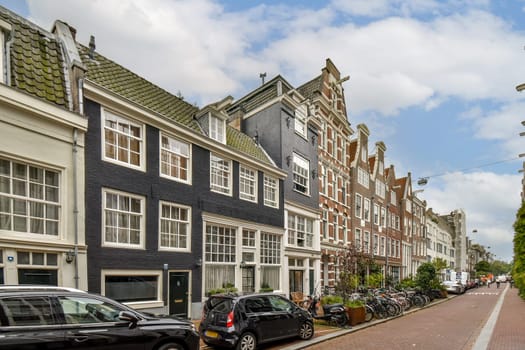 Distinctive buildings line a canal in Amsterdam, showcasing a blend of historical and modern architectural styles under a bright blue sky.