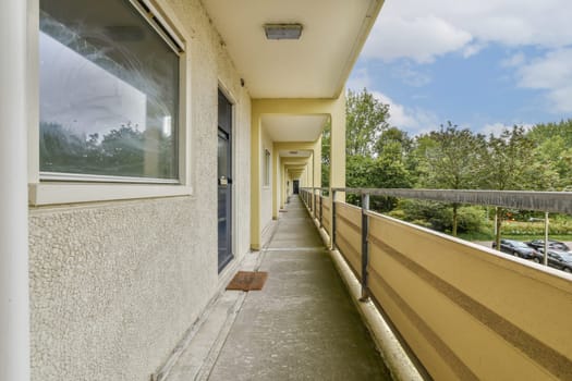 A view down a modern apartment corridor featuring a glimpse of greenery outside through large windows. The space is designed with clean lines and natural light.