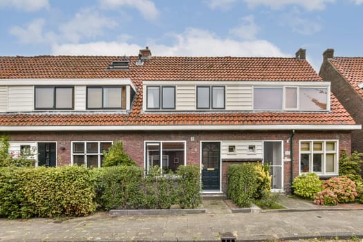 A picturesque two-story house featuring a welcoming entrance, neatly trimmed hedges, and a vibrant garden, surrounded by a tranquil neighborhood setting.