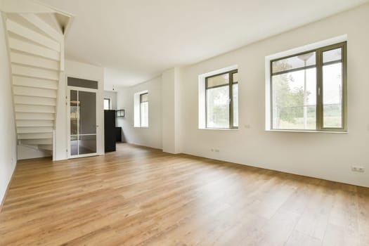 Bright, minimalist interior showcases natural light flowing through large windows, featuring wooden flooring and a contemporary staircase design.