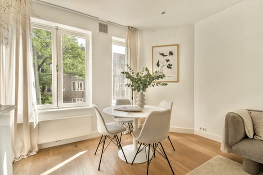 A stylish dining area featuring a round table surrounded by elegant chairs, large windows letting in natural light, and a touch of greenery.