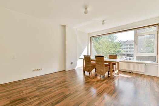 A spacious minimalistic room featuring wooden floors, natural light streaming through large windows, and a simple furniture arrangement creating a serene atmosphere.