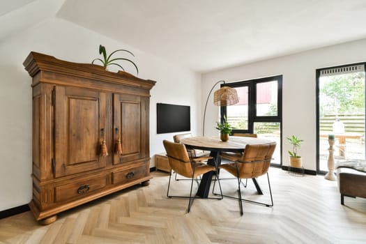 Stylish living room featuring a wooden cabinet, elegant furniture, and natural light streaming through large windows, creating a warm and inviting atmosphere.