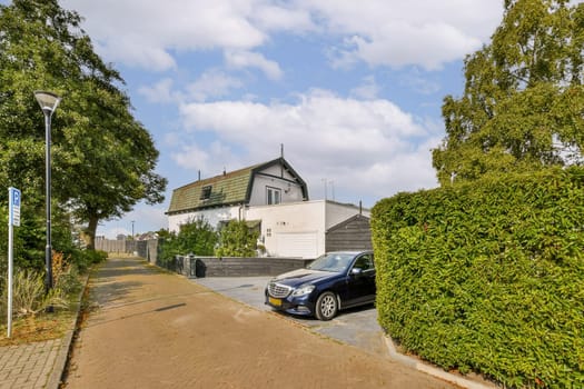 A picturesque view of a residential area showcasing a car parked by a house amidst lush greenery and a clear blue sky.