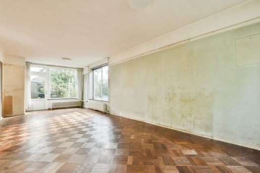 An expansive empty room featuring large windows that allow ample natural light, showcasing a light wood floor and bare walls ready for decoration.