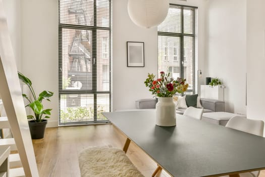 A stylish modern living space featuring natural light, a minimalist table, potted plants, and decorative flowers in a vase, highlighting comfort and elegance.