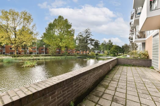 A tranquil view showcasing a riverside pathway lined with trees and residential buildings in the background, capturing the essence of nature in an urban setting.