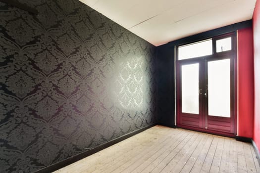 A spacious empty hallway featuring ornate dark wallpaper and a large door that allows light to enter, enhancing the contrast with the walls.