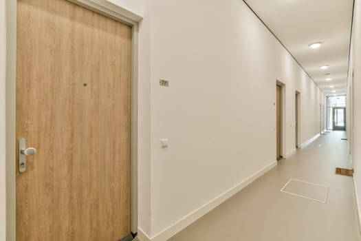 A spacious and well-lit indoor hallway featuring wooden doors on either side, minimalist design, and clean lines, inviting warmth and comfort.