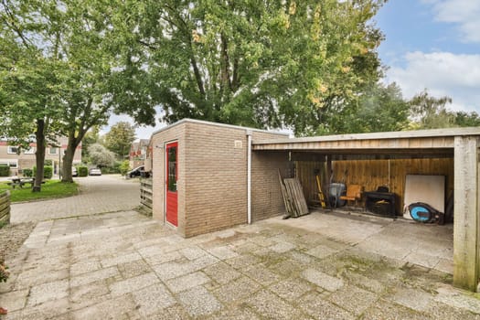 A stylish outdoor storage shed with a red door, surrounded by lush greenery and a paved pathway, creating a serene urban environment.