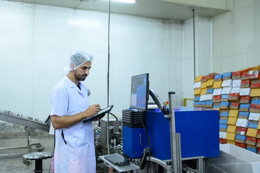 Factory worker in food processing plant monitoring production data on computer.