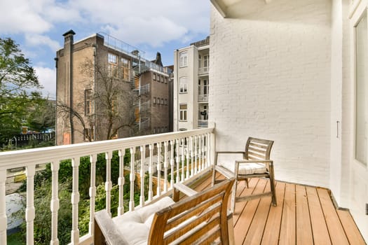 A cozy balcony with wooden flooring, a comfortable chair, and a view of greenery and neighboring buildings creates a serene urban retreat.