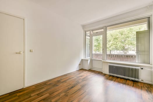 A minimalist interior featuring a large window allowing natural light to flood the room. The wooden floor adds warmth to the space, enhancing its inviting atmosphere.