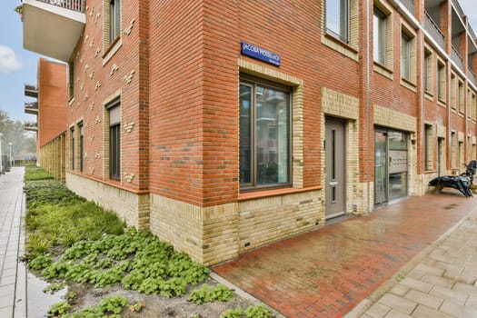 This illustration showcases a contemporary red brick building facade with large windows and greenery surrounding the entrance, emphasizing architectural design.