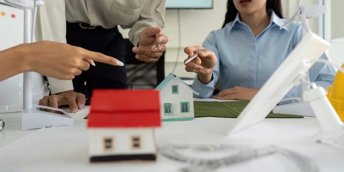 Professionals are in a meeting focused on sustainable housing solutions, analyzing mini models while highlighting the importance of renewable energy in modern architecture.