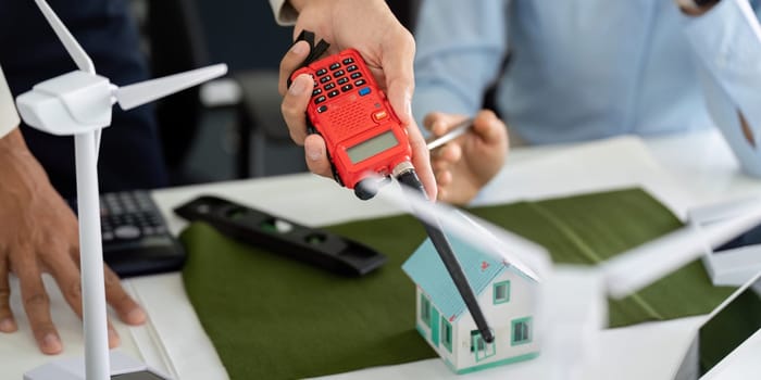 In a collaborative environment, a young professional uses a device to assess sustainability metrics for a model house, showcasing sustainable engineering practices.