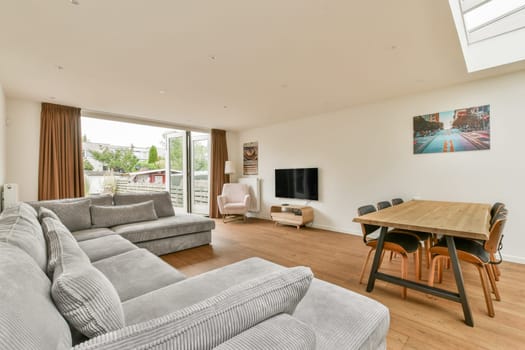 A stylish and contemporary living room featuring a comfortable sofa, dining area, and large windows with natural light flowing in. The minimalist decor enhances the space.