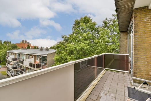 Spacious balcony overlooking lush greenery and modern architecture, featuring glass railing and stone flooring. An inviting outdoor space for relaxation.