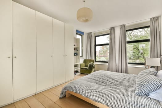 A contemporary bedroom featuring a neatly made bed, large windows allowing natural light, and stylish furniture. The minimalist design enhances comfort and relaxation.