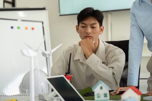 A focused individual reviews architectural models and sustainable energy solutions, contemplating innovative approaches in a collaborative workspace.