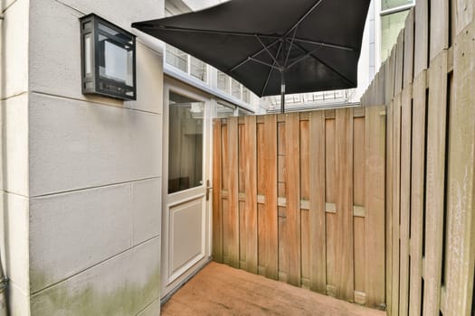 A stylish modern outdoor area featuring a wooden fence, a black umbrella, and a sleek door, creating an inviting ambiance. Ideal for relaxation or small gatherings.
