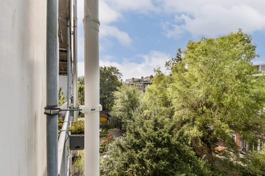An inviting view from an urban balcony showcasing vibrant trees and plants, contrasting with a modern building structure under a blue sky.