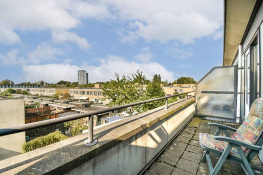 A serene urban balcony showcasing colorful furniture, overlooking a neighborhood filled with buildings and greenery under a cloudy sky.