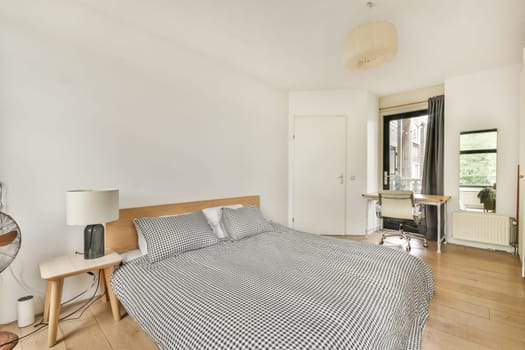 A contemporary bedroom featuring a large bed with checkered bedding, minimalist furnishings, and natural light pouring in through large windows.
