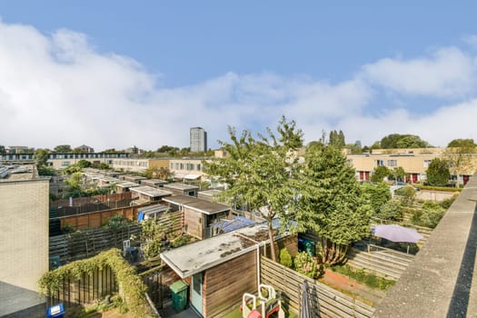 A panoramic view showcasing a tranquil urban garden area surrounded by residential buildings under a clear blue sky. A blend of greenery and architecture.