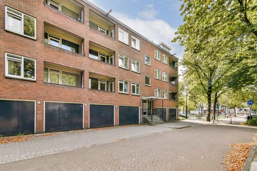 A contemporary apartment complex featuring a brick exterior, positioned amidst green trees and a well-maintained pathway leading to the entrance.