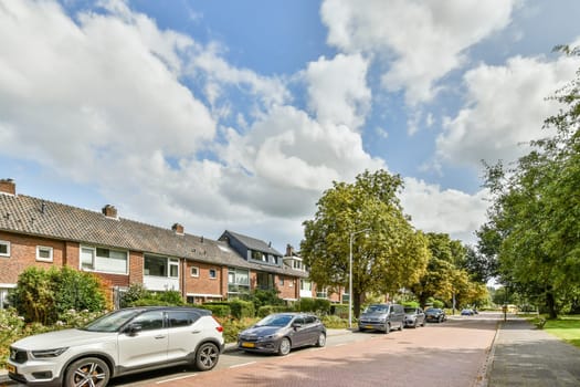 A picturesque residential street showcasing well-maintained houses, lush trees, and parked cars under a partly cloudy sky.