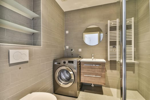 A sleek modern bathroom featuring a combination of grey tiles, a washing machine, and stylish fixtures, enhancing the contemporary home aesthetic.
