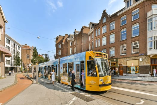 A brightly colored tram stops in a lively city street with pedestrians interacting near historic buildings.
