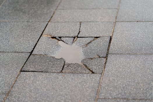Destroyed sidewalk slab with a puddle of rainwater on a sidewalk in the city center of Swinoujscie, Swinoujscie in Poland