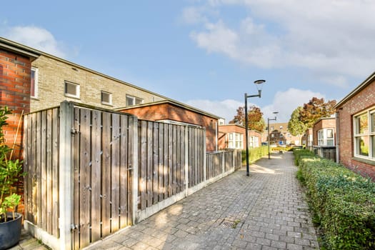 A picturesque alleyway surrounded by modern buildings, featuring wooden fences, well-maintained sidewalks, and hints of green landscaping.